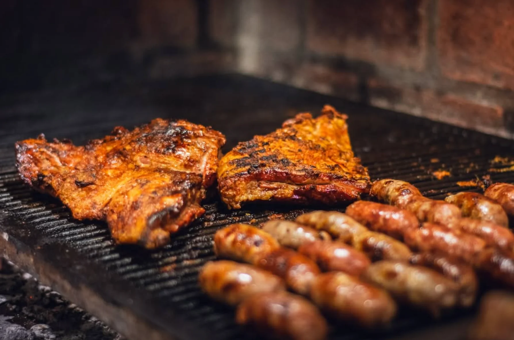 Asado de tira y chorizos dorándose sobre la parrilla de Herencia
